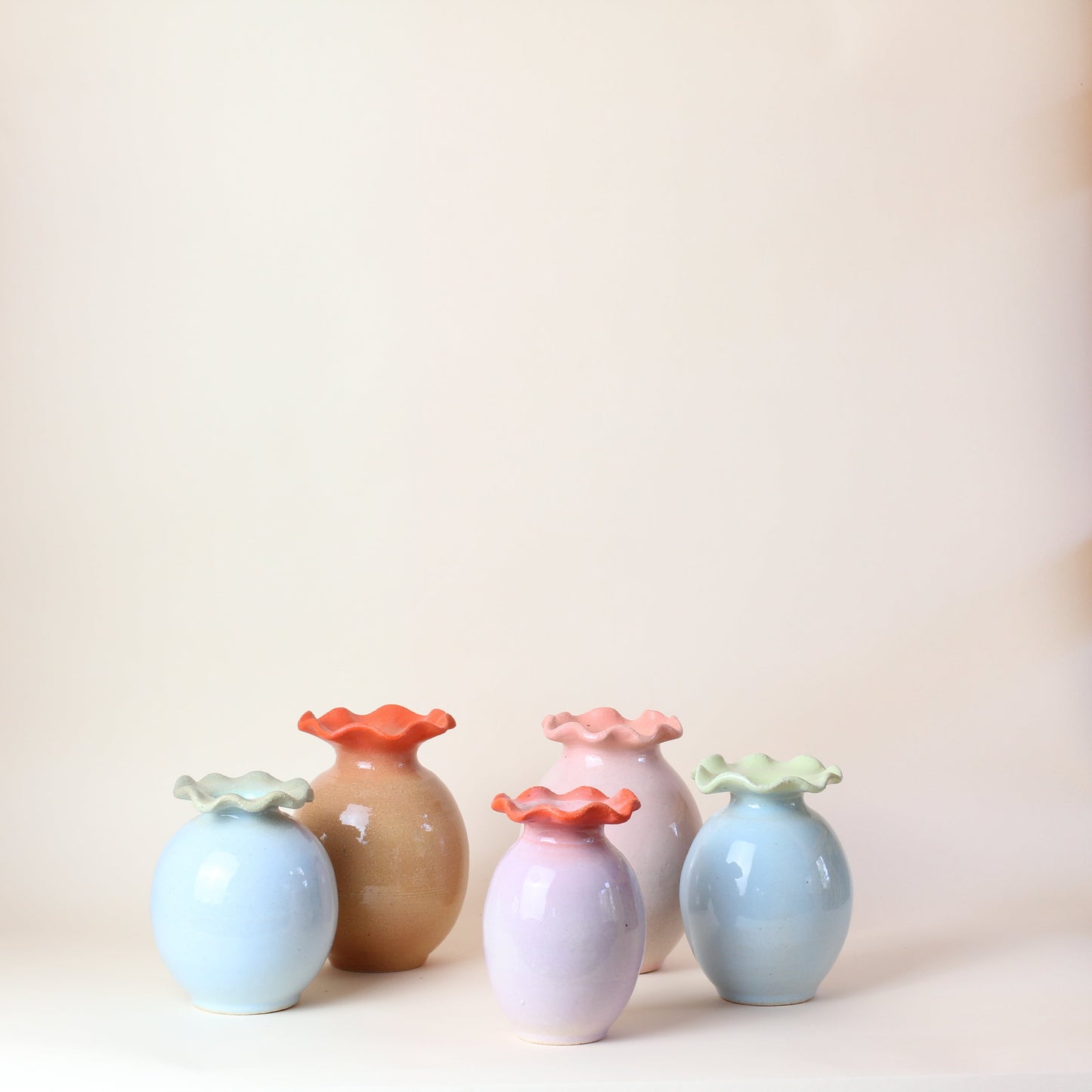 Set of colorful ceramic vases on a white surface with wooden shelves in the background